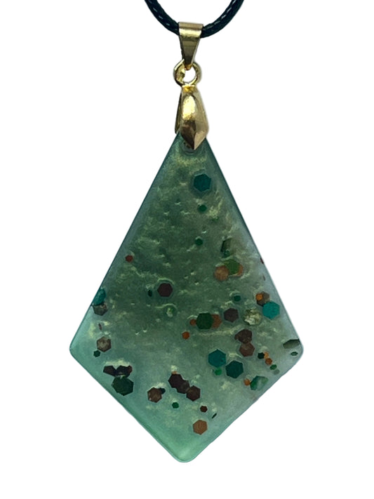 Handcrafted frosted semi-translucent celadon resin elongated diamond kite pendant with bold scattered hexagonal glitter pieces in deep teal, burnt orange, copper, forest green, and burgundy, suspended from a black braided cord with a gold-toned bail.