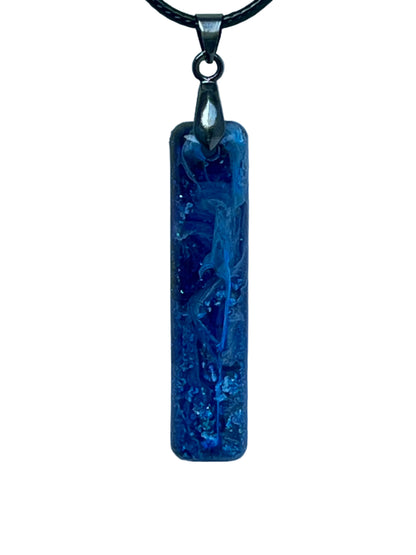 Handcrafted rich opaque royal blue resin tall narrow bar pendant with luminous white swirl formations and fine iridescent glitter throughout, suspended from a black braided cord with a gunmetal bail.
