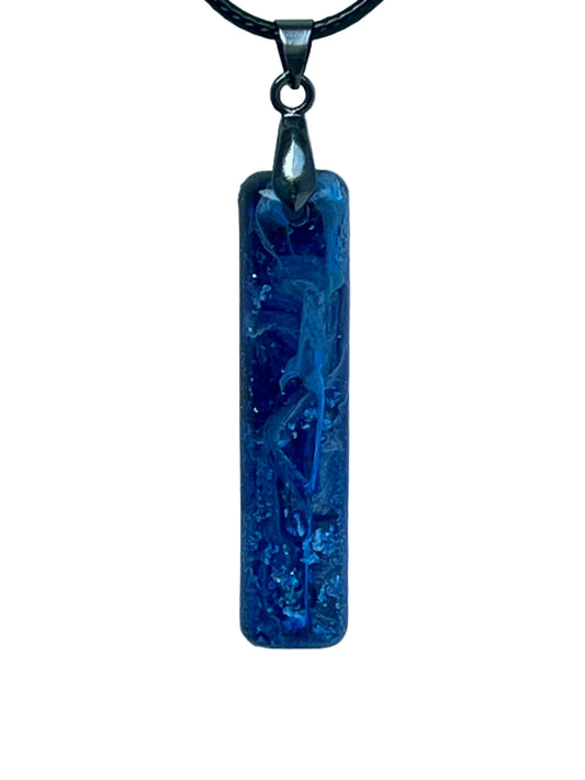 Handcrafted rich opaque royal blue resin tall narrow bar pendant with luminous white swirl formations and fine iridescent glitter throughout, suspended from a black braided cord with a gunmetal bail.
