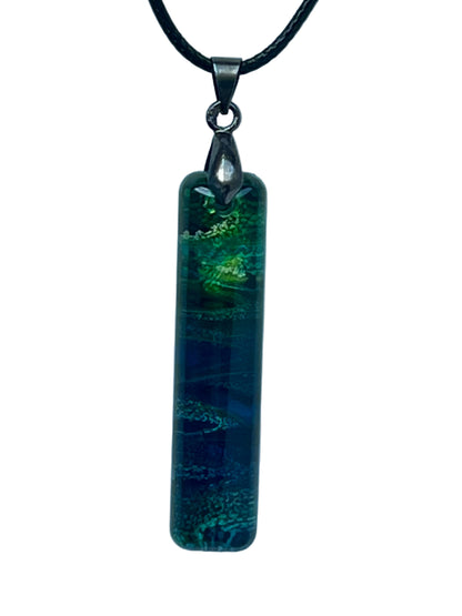 Handcrafted layered teal and sapphire blue resin tall narrow bar pendant with an electric chartreuse and acid-green glitter burst at the upper portion and fine iridescent shimmer throughout, suspended from a black braided cord with a gunmetal bail.