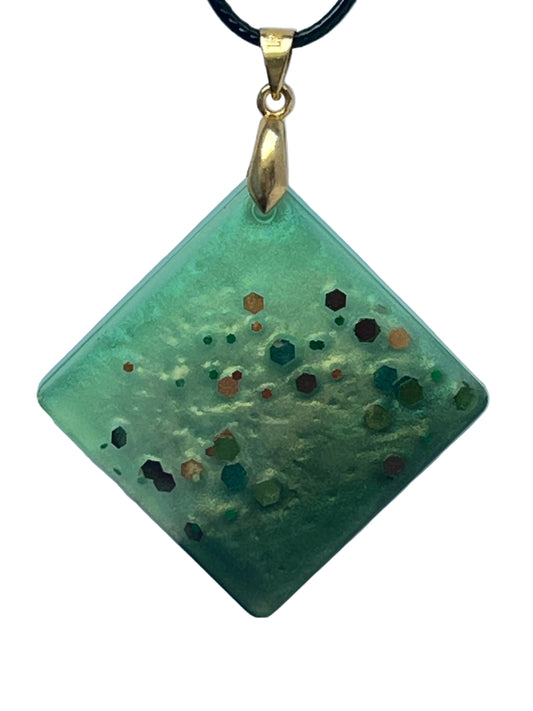 Handcrafted frosted semi-translucent celadon and sage green resin square diamond pendant with bold scattered hexagonal glitter pieces in burnt orange, copper, burgundy, forest green, and teal, suspended from a black braided cord with a gold-toned bail.