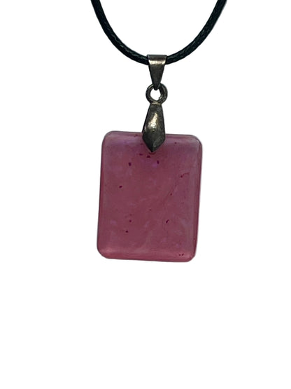 Handcrafted soft semi-translucent blush mauve resin small rounded square pendant with scattered tiny deep magenta and violet flecks, suspended from a black braided cord with a gunmetal bail.