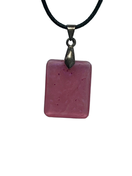 Handcrafted soft semi-translucent blush mauve resin small rounded square pendant with scattered tiny deep magenta and violet flecks, suspended from a black braided cord with a gunmetal bail.