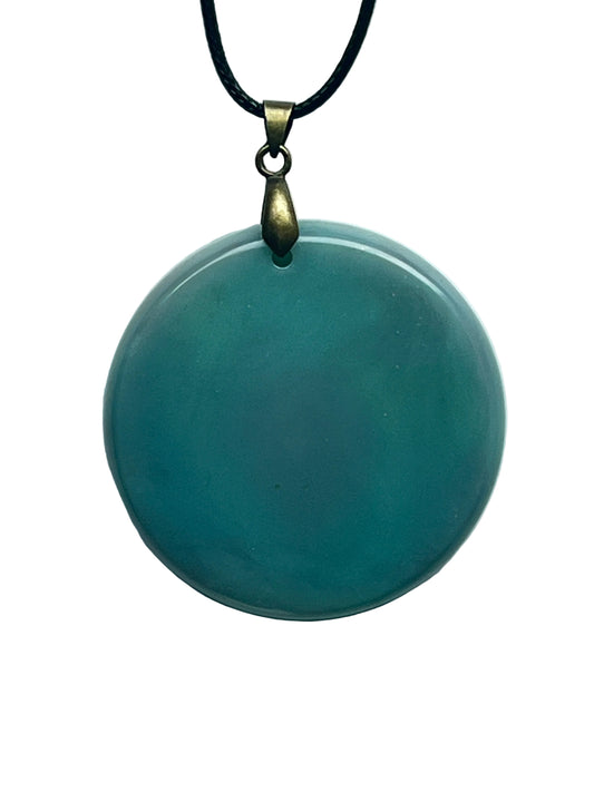 Handcrafted rich opaque dusty teal resin large circle pendant with a smooth glassy high-gloss finish, suspended from a black braided cord with an antiqued brass bail.