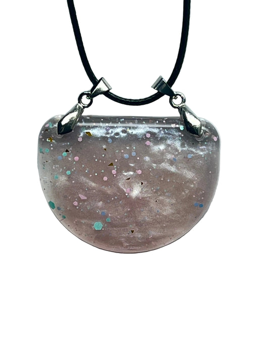 Handcrafted soft dusty mauve pearlescent resin wide half-moon bib pendant with scattered multicolor confetti glitter in blush pink, iridescent lavender, mint teal, gold triangles, and fine silver-white micro-glitter, suspended from a black braided cord with two silver-toned bails.