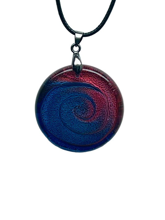 Handcrafted resin large circle pendant with a saturated crimson red outer rim sweeping inward in a dramatic spiral to a deep cobalt and sapphire blue center, with rich textured shimmer throughout, suspended from a black braided cord with a silver-toned bail.