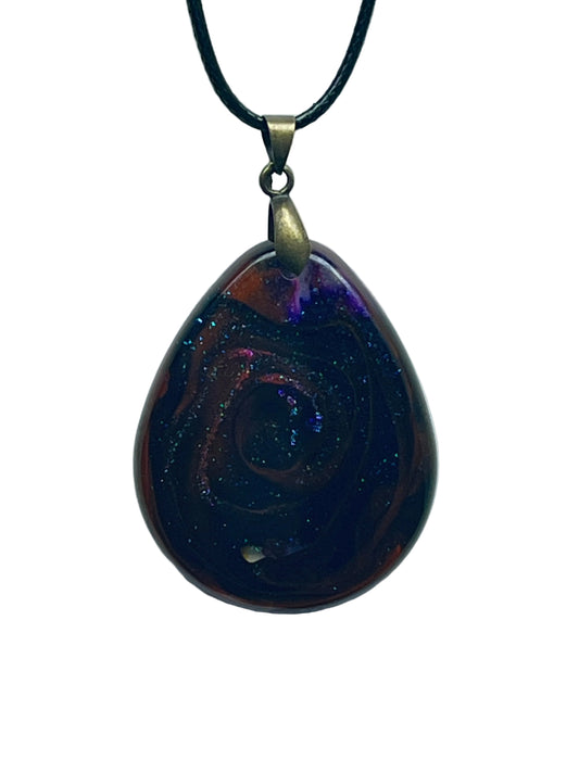 Handcrafted deep near-black resin generous teardrop pendant with swirling crimson and auburn undercurrents, fine iridescent blue-violet galaxy glitter throughout, and an electric violet-blue nebula burst at the upper portion, suspended from a black braided cord with an antiqued brass bail.