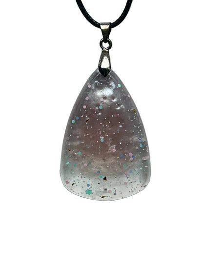 A teardrop-shaped resin pendant that fades from a soft dusty mauve at the top to frosted clear white at the rounded base, scattered with confetti flecks in pink, mint, blue, and gold. It hangs from a silver-toned bail on a black braided cord against a pale background.