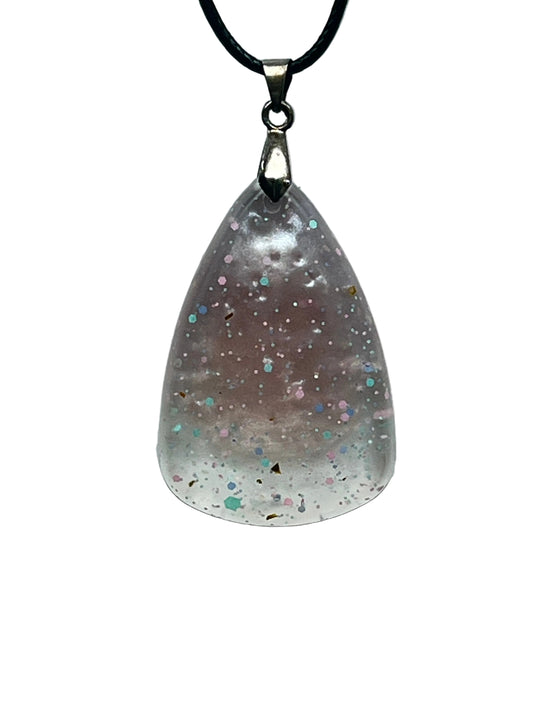 A teardrop-shaped resin pendant that fades from a soft dusty mauve at the top to frosted clear white at the rounded base, scattered with confetti flecks in pink, mint, blue, and gold. It hangs from a silver-toned bail on a black braided cord against a pale background.