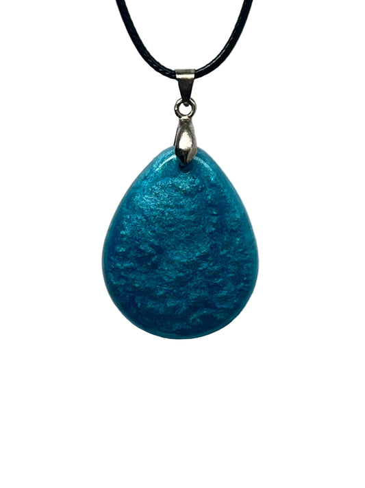 A smooth teardrop-shaped resin pendant in shimmering teal and aqua blue with a frosted, mottled, water-like texture and pearlescent currents. It hangs from a silver-toned bail on a black braided cord against a pale background.