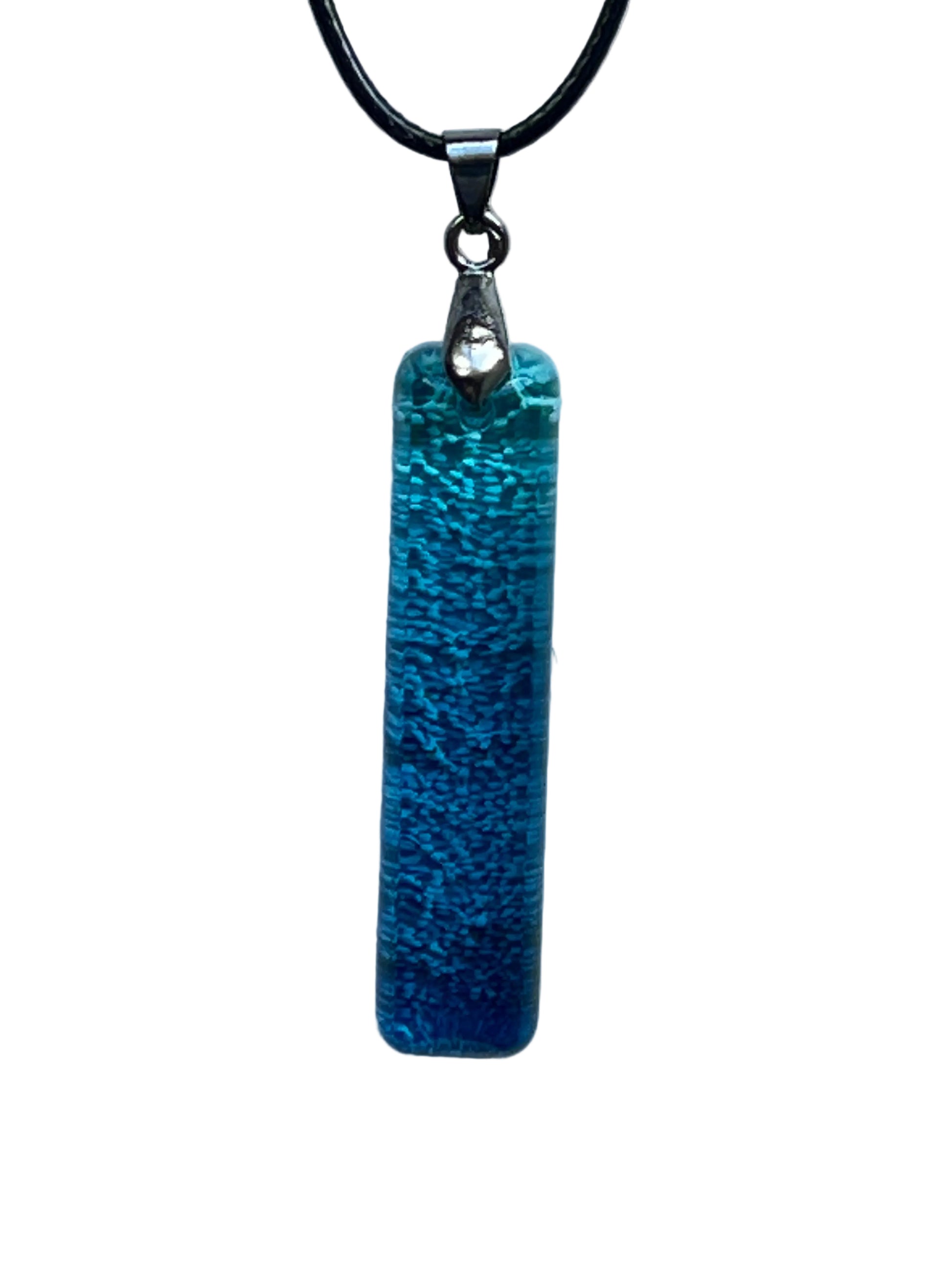 A slender vertical bar-shaped resin pendant with a finely textured, frosted surface in a gradient from bright turquoise and aqua at the top to deep ocean blue at the base. It hangs from a gunmetal bail on a black braided cord against a pale background.