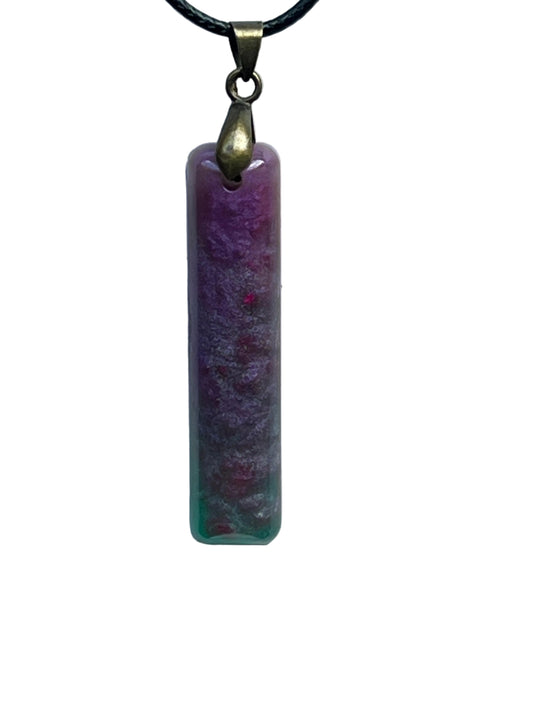 A slender vertical bar-shaped resin pendant with a frosted texture and a soft gradient from orchid purple and magenta at the top to sea-green and jade at the base. It hangs from an antiqued brass bail on a black braided cord against a pale background.