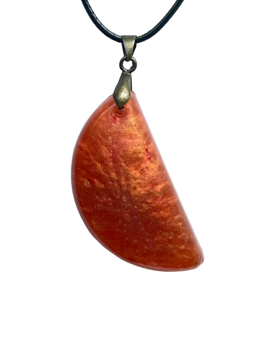 A half-circle (half-moon) shaped resin pendant in rich, fiery orange with mottled, flame-like tones of tangerine, marigold, and burnt amber. It hangs from an antiqued brass bail on a black braided cord against a pale background.