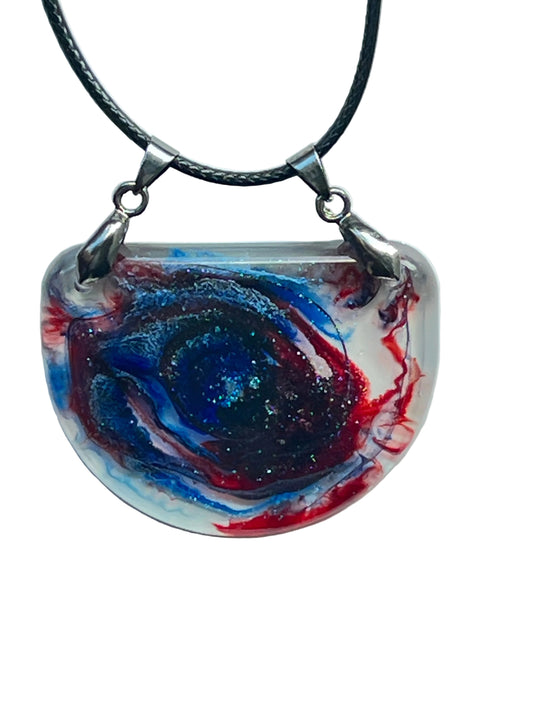 A half-circle (half-moon) shaped resin pendant with a swirling galaxy-like design of deep crimson red and cobalt blue spiraling around a dark glittering center, fading into clear resin at the edges. It hangs from two gunmetal bails on a black braided cord against a pale background.