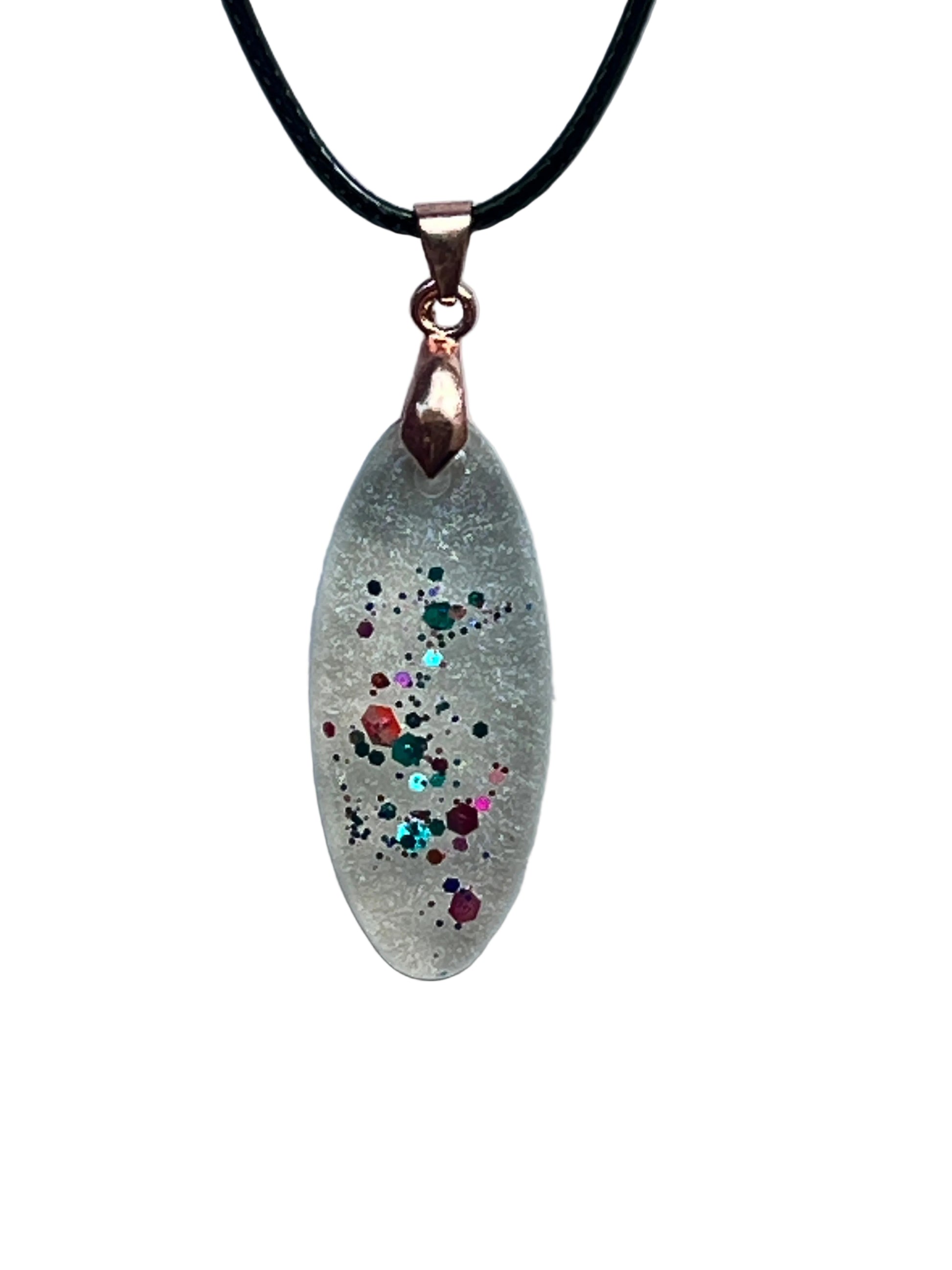 An elongated marquise-shaped frosted clear resin pendant with a ribbon of multicolored confetti flecks — green, red, orange, pink, and aqua with gold sparkle — scattered down the center. It hangs from a rose gold bail on a black braided cord against a pale background.
