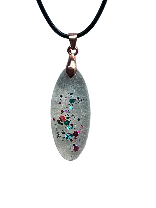 An elongated marquise-shaped frosted clear resin pendant with a ribbon of multicolored confetti flecks — green, red, orange, pink, and aqua with gold sparkle — scattered down the center. It hangs from a rose gold bail on a black braided cord against a pale background.