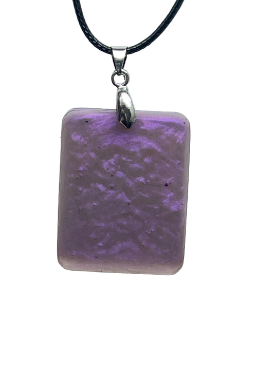 A rectangular resin pendant in soft lilac with a frosted matte finish and swirling, cloud-like blooms of deeper violet purple throughout. It hangs from a silver-toned bail on a black braided cord against a pale background.