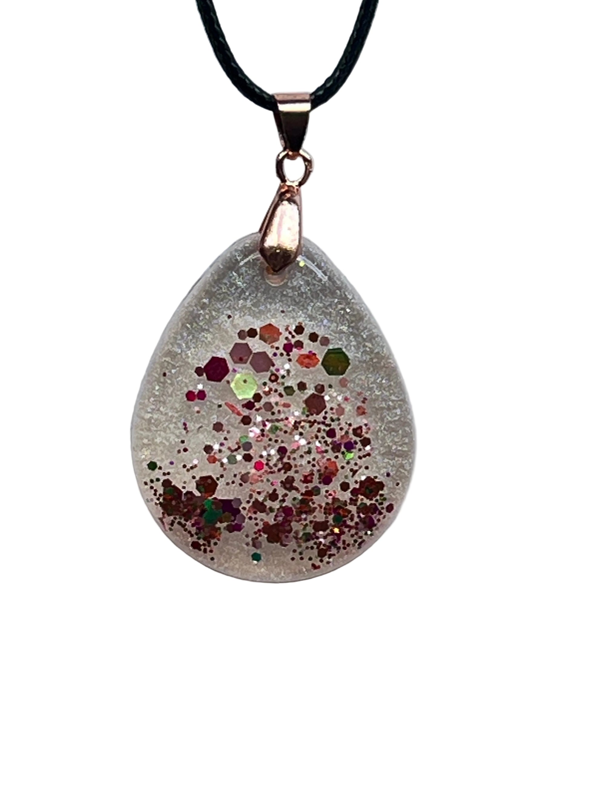 A teardrop-shaped frosted clear resin pendant with a burst of multicolored confetti — copper, rose-gold, ruby, lime green, fuchsia, and silver glitter — clustered through the lower half. It hangs from a rose gold bail on a black braided cord against a pale background.