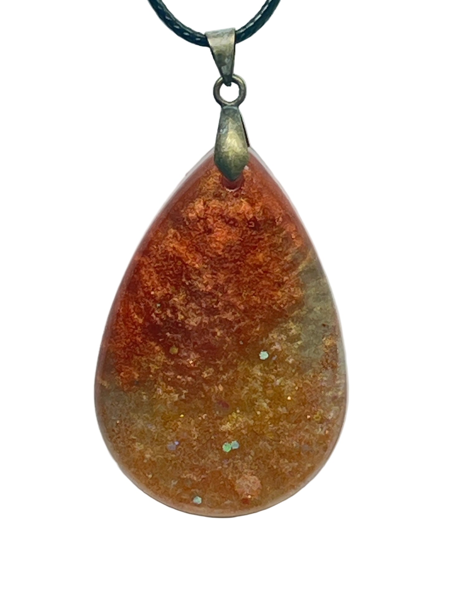 A teardrop-shaped resin pendant with a warm gradient from deep rust at the top to amber and honey-gold at the base, scattered with small iridescent opal flecks. It hangs from an antiqued brass bail on a black braided cord against a pale background.