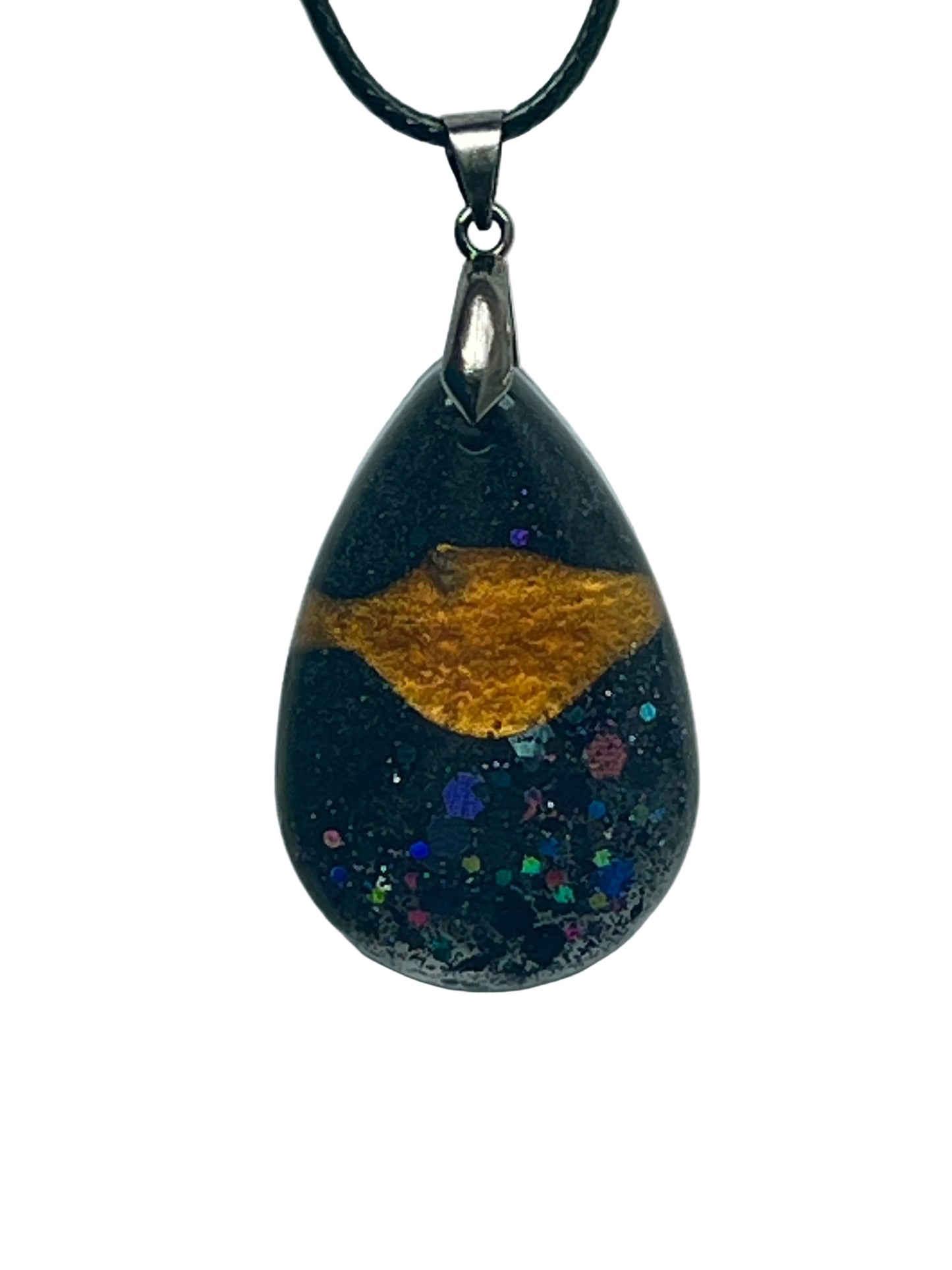 A teardrop-shaped resin pendant with a deep black base, a streak of molten gold across the upper half, and a scatter of iridescent rainbow confetti hexagons across the lower half like stars. It hangs from a gunmetal bail on a black braided cord against a pale background.
