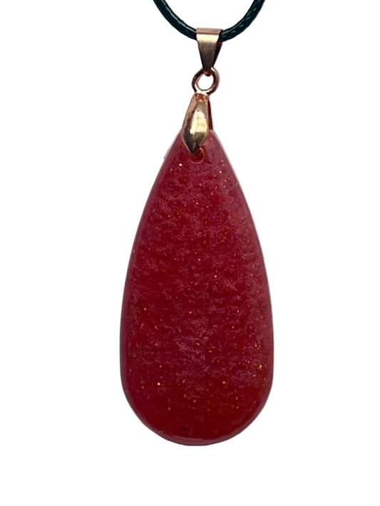 An elongated teardrop-shaped resin pendant in deep crimson-scarlet red with a soft frosted texture and scattered fine gold sparkle flecks throughout. It hangs from a rose gold bail on a black braided cord against a pale background.