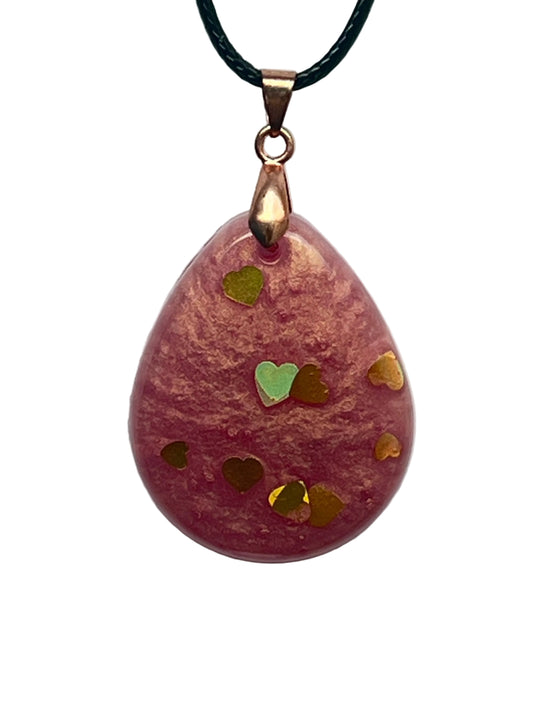 A teardrop-shaped resin pendant in dusty rose pink with warm coppery-gold tones, scattered with small gold and copper heart-shaped confetti and one iridescent mint-green heart. It hangs from a rose gold bail on a black braided cord against a pale background.