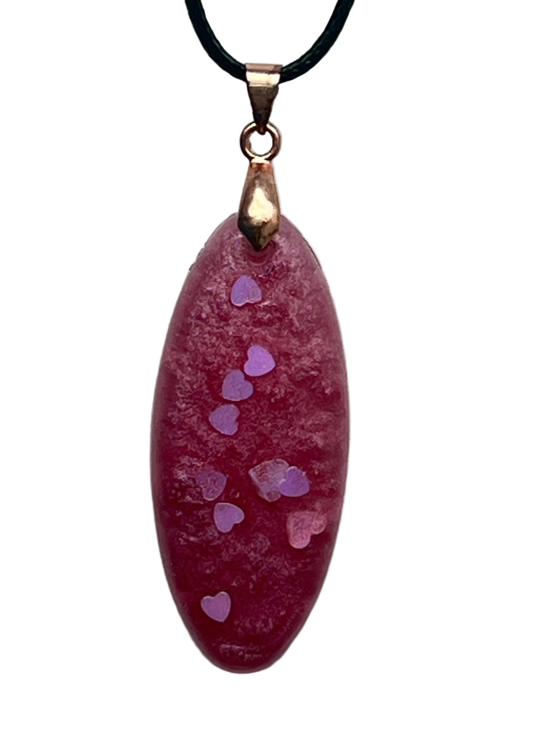 An elongated oval-shaped resin pendant in dusty mauve-rose with a frosted texture and a trail of small lilac and iridescent heart-shaped confetti drifting down the center. It hangs from a rose gold bail on a black braided cord against a pale background.