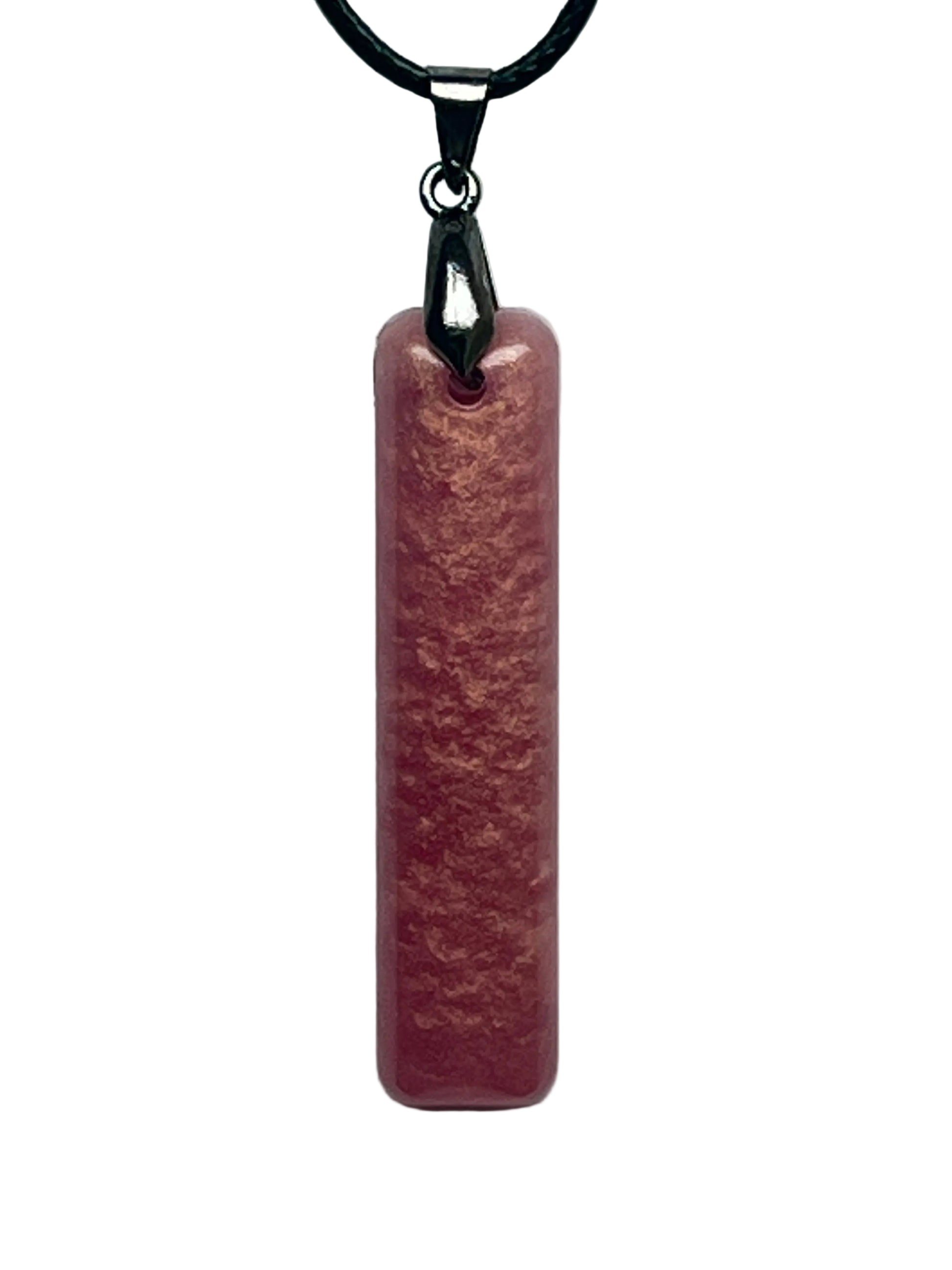 A slender vertical bar-shaped resin pendant in warm mauve-rose with a velvety suede-like texture and coppery, peach-toned mottling throughout. It hangs from a gunmetal bail on a black braided cord against a pale background.