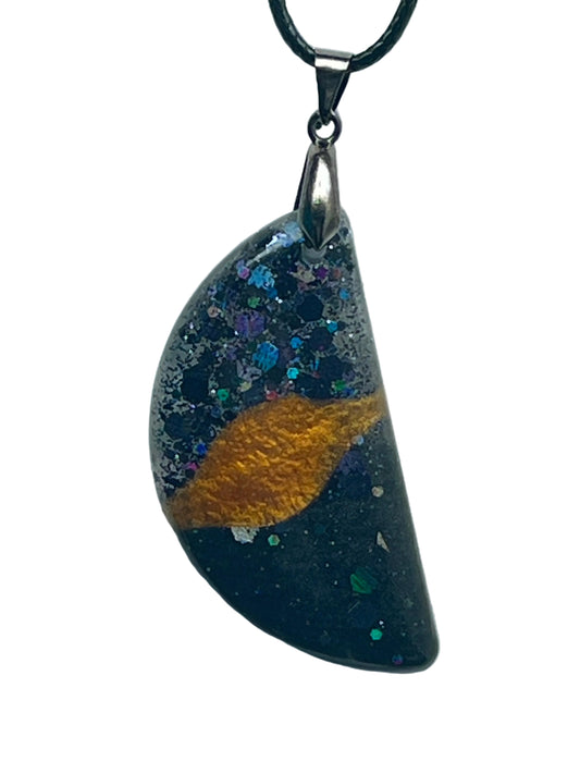 A half-circle (half-moon) shaped resin pendant with a deep cosmic-black base, a sweeping band of molten gold across the center like planetary rings, and scattered iridescent blue, violet, green, and silver confetti like stars. It hangs from a gunmetal bail on a black braided cord against a pale background.