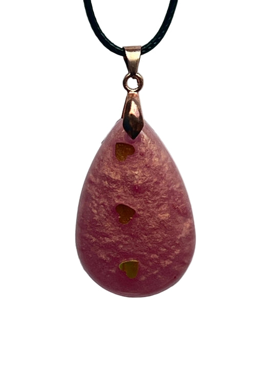 A teardrop-shaped resin pendant in dusty rose pink with a frosted texture and warm coppery-gold tones, with three gold heart-shaped confetti pieces lined up vertically down the center. It hangs from a rose gold bail on a black braided cord against a pale background.