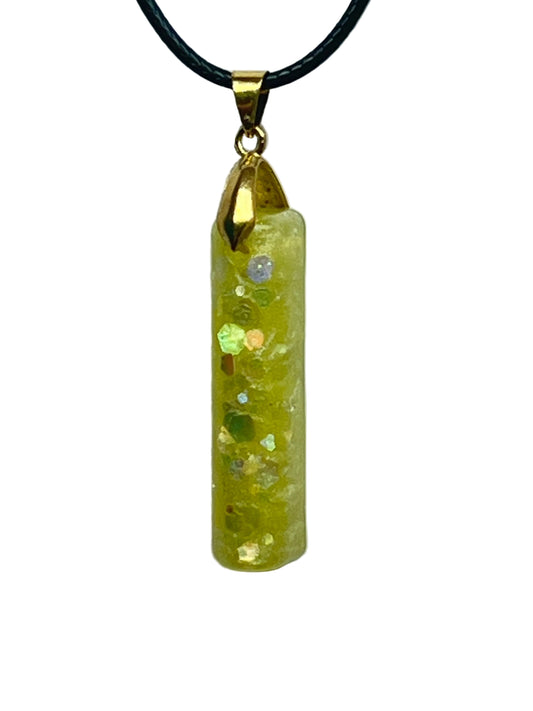 A slender vertical bar-shaped resin pendant in bright sunny yellow with crackled sparkle and scattered iridescent green, gold, and silver confetti hexagon flecks. It hangs from a gold-toned bail on a black braided cord against a pale background.