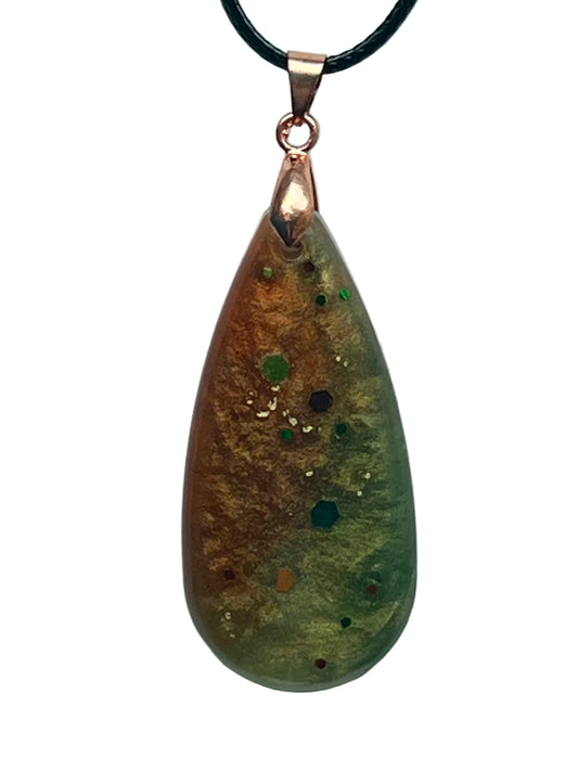 An elongated teardrop-shaped resin pendant with a shimmering gradient from warm copper and gold on one side to olive and sage green on the other, scattered with emerald, teal, burgundy, and copper confetti hexagon flecks. It hangs from a rose gold bail on a black braided cord against a pale background.