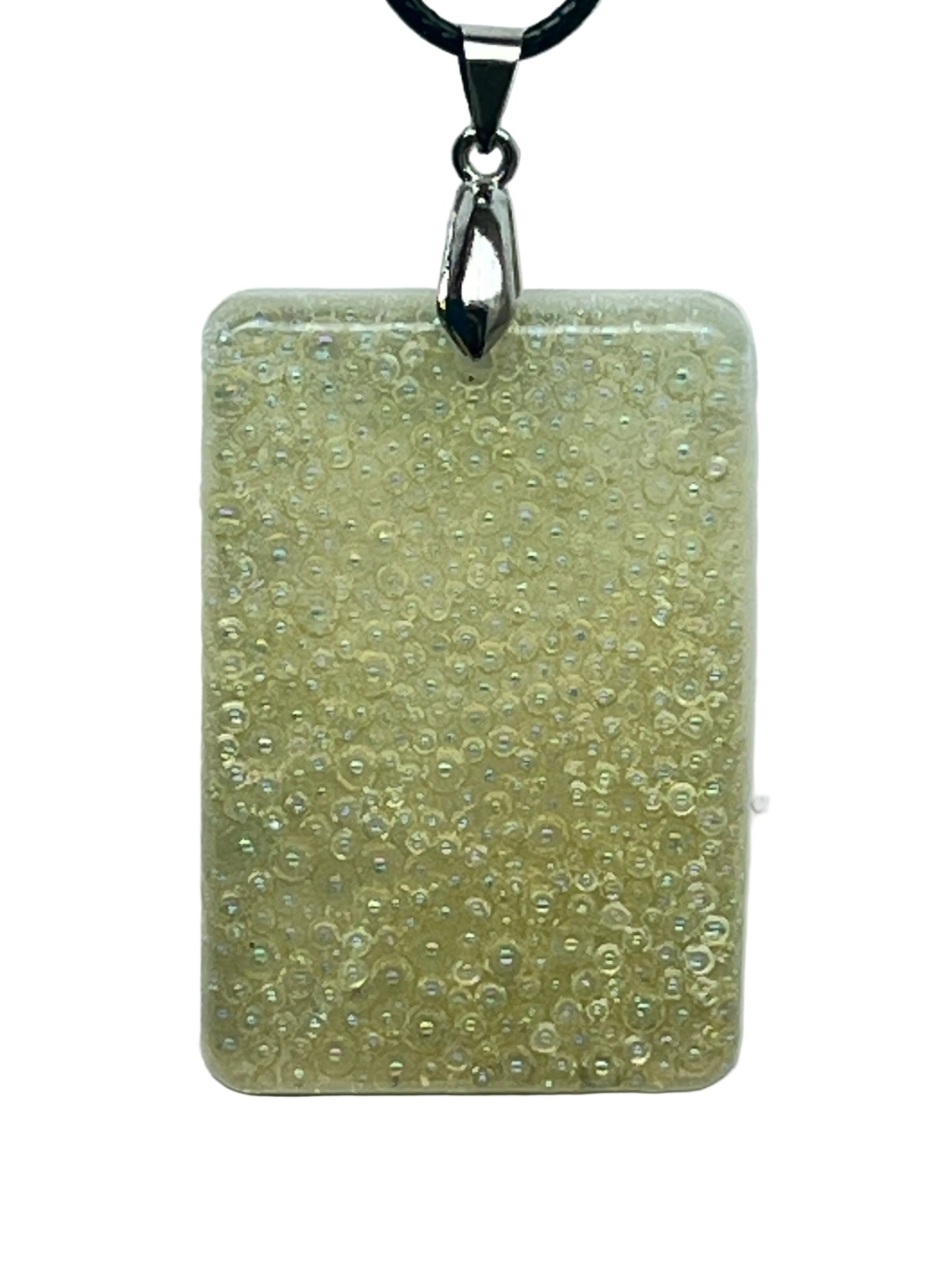 A rectangular resin pendant in creamy ivory and pale gold, packed completely full of tiny iridescent bubble-beads and micro-pearls with a soft opal shimmer. It hangs from a silver-toned bail on a black braided cord against a pale background.