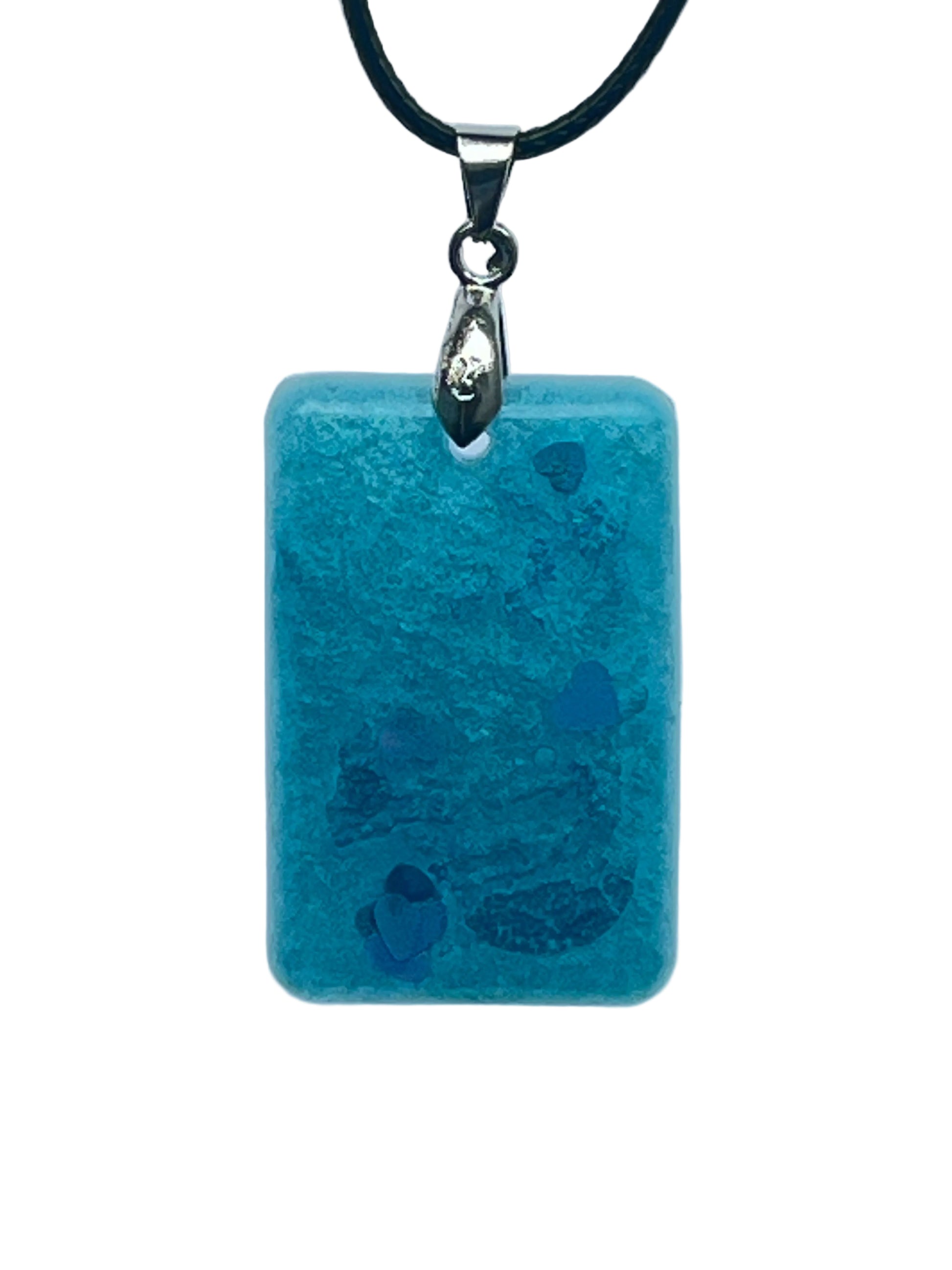 A rectangular resin pendant in frosted aqua and teal blue with a mottled, watery texture, scattered across the lower half with blue and iridescent heart-shaped confetti. It hangs from a silver-toned bail on a black braided cord against a pale background.
