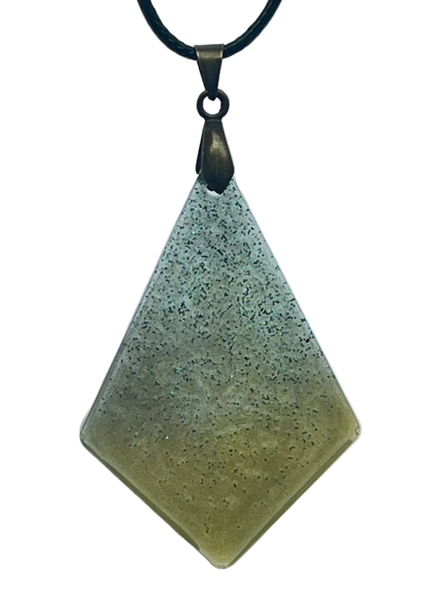 A kite-shaped (elongated diamond) resin pendant with a gradient from cool sage-grey at the top to warm olive-green at the base, scattered throughout with fine dark green glitter. It hangs from an antiqued brass bail on a black braided cord against a pale background.