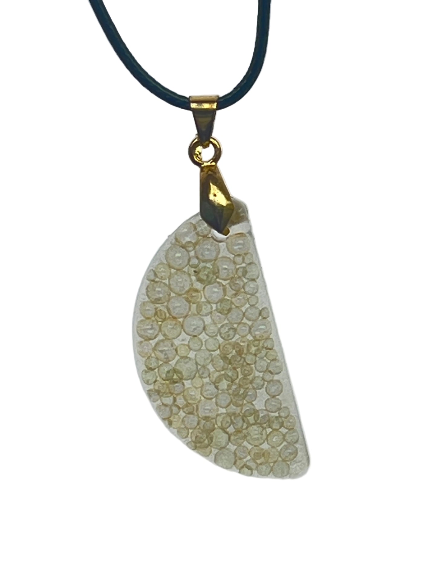An organically curved, freeform resin pendant in soft ivory and cream, densely packed with tiny round bubble-bead inclusions that catch the light. It hangs from a gold-toned bail on a black braided cord against a pale background.
