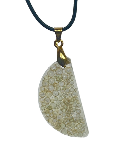 An organically curved, freeform resin pendant in soft ivory and cream, densely packed with tiny round bubble-bead inclusions that catch the light. It hangs from a gold-toned bail on a black braided cord against a pale background.