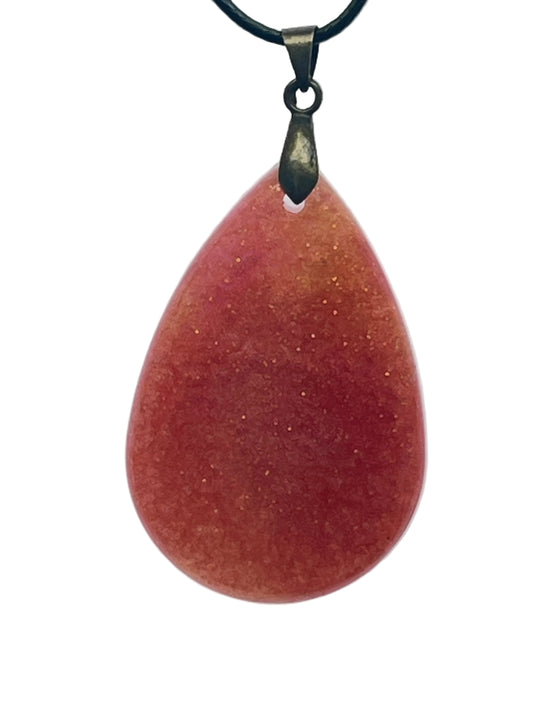 A full, rounded teardrop-shaped resin pendant in deep rust red with warm coral undertones near the top, scattered throughout with fine gold sparkle. It hangs from an antiqued brass bail on a black braided cord against a pale background.