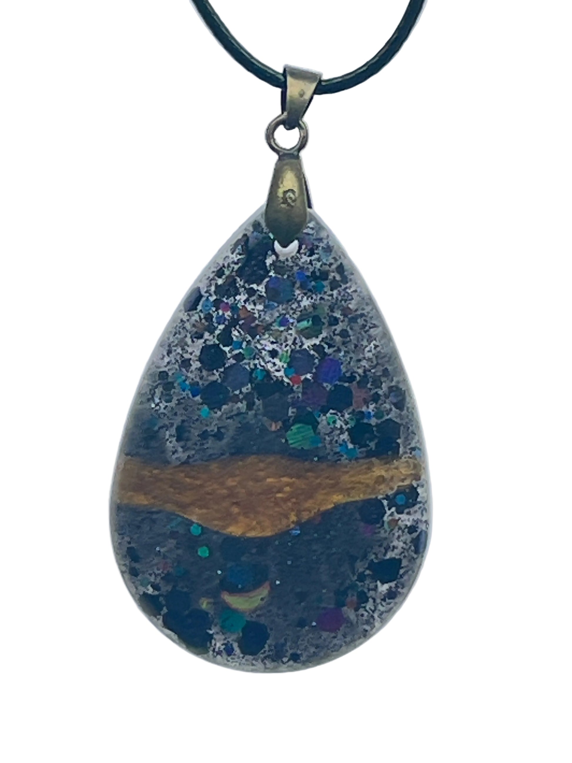 A teardrop-shaped resin pendant with a horizontal band of amber-gold across the center, framed above and below by dense cosmic speckle in black, deep blue, violet, teal, and silver. It hangs from an antiqued brass bail on a black braided cord against a pale background.