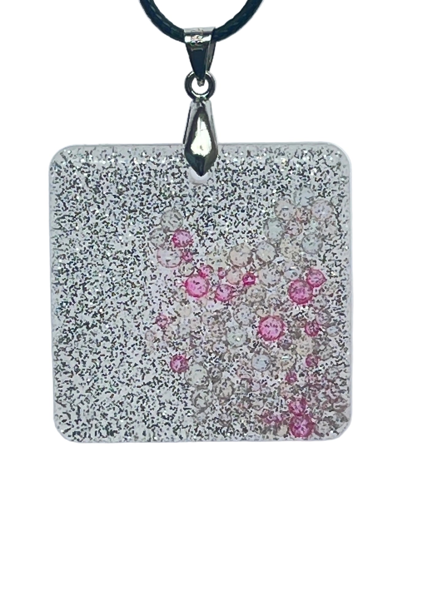 A square-shaped resin pendant densely covered in fine silver glitter, with a cluster of clear and rose-pink bubble-bead inclusions drifting near the center. It hangs from a silver-toned bail on a black braided cord against a pale background.