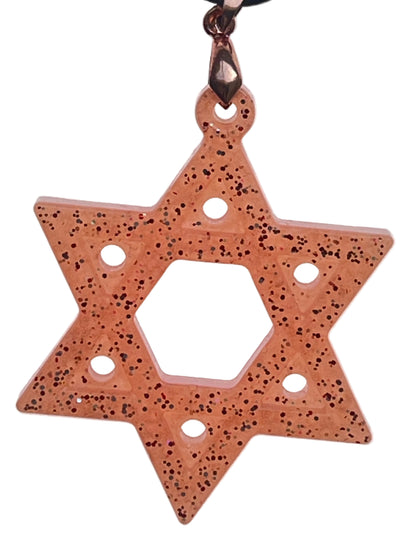 A six-pointed star (hexagram) resin pendant in warm peachy-amber with fine dark copper and black glitter throughout, featuring an open hexagonal center and circular cut-out windows at each point. It hangs from an antiqued brass bail on a black braided cord against a pale background.