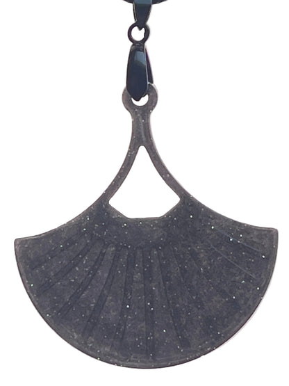 A fan or leaf-shaped resin pendant in deep charcoal grey with fine silver glitter throughout, featuring ribbed vein-like detailing and a small triangular cut-out near the top. It hangs from a gunmetal bail on a black braided cord against a pale background.