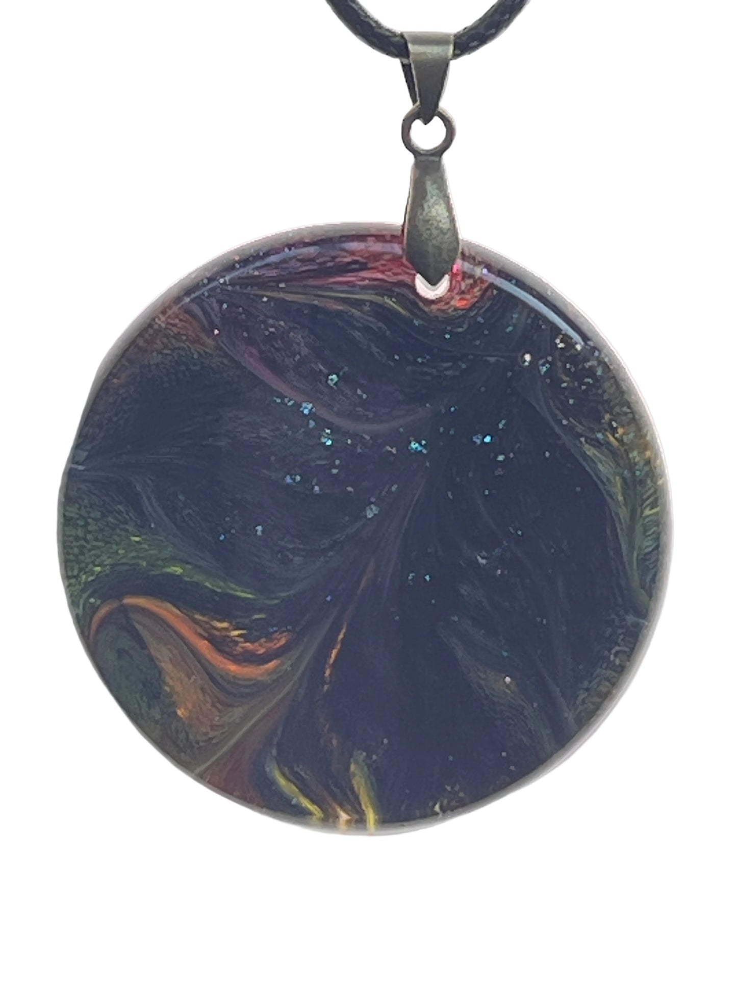 A large round resin pendant with a deep, swirling near-black base dusted with fine glitter, and glimpses of amber, orange, crimson, and jade green along the edges. It hangs from a gunmetal bail on a black braided cord against a pale background.
